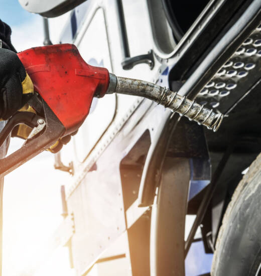 A worker refills a heavy-duty truck with fuel at a service station during sunset, showcasing the importance of logistics and transportation.